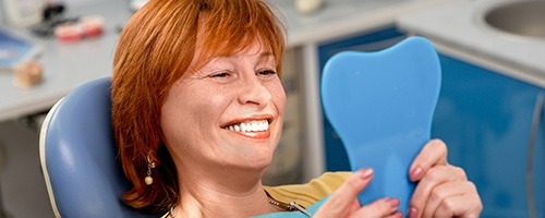 Older woman in dental chair looking at smile in mirror