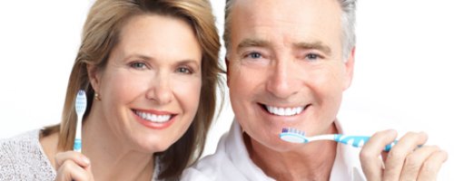 An older couple smiling and holding toothbrushes.