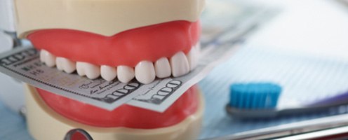A jaw mockup biting money sitting next to dental tools