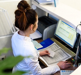 A female dental receptionist sitting behind a computer waiting for the next patient to arrive
