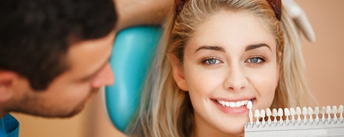 A dentist using a shade guide to compare with a patient’s smile