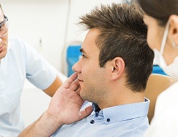 Man in dental chair holding cheek in dental emergency