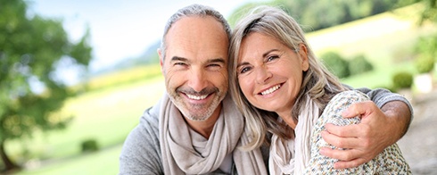 Middle-aged couple smiling together while sitting outside