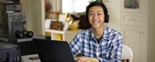 a teen using their laptop at the kitchen table and smiling