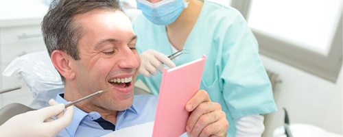 A man looking at his smile in the mirror at the dentist’s office