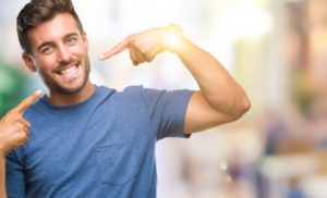 young man pointing to his smile after seeing his cosmetic dentist 