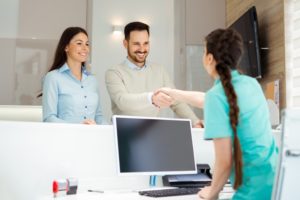 dental team member shaking hands with patient at front desk 