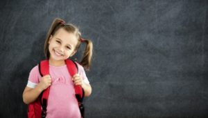 little girl smiling after visiting a children’s dentist and wearing a backpack