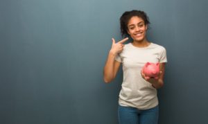 young woman holding a piggy bank and pointing to her smile 
